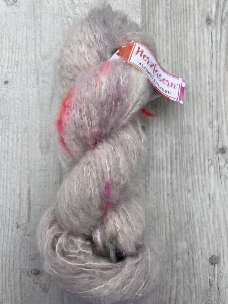 „Flauschiger Strang aus Baby-Suri-Alpaka und Seide in nebligen Grau- und Beigetönen mit Pink- und Grünakzenten; fotografiert auf hellem Holzuntergrund mit Herzfasern-Etikett.“